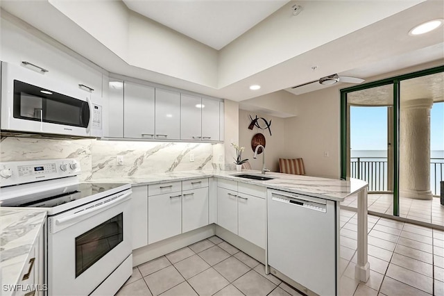 kitchen with light tile patterned flooring, sink, white cabinetry, kitchen peninsula, and white appliances