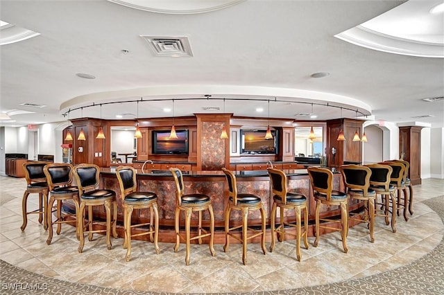 bar with light tile patterned flooring, ornate columns, crown molding, decorative light fixtures, and a raised ceiling