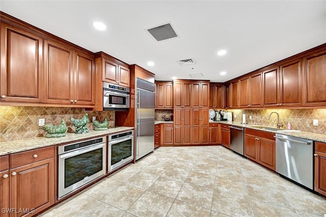 kitchen with sink, light tile patterned floors, backsplash, stainless steel appliances, and light stone counters