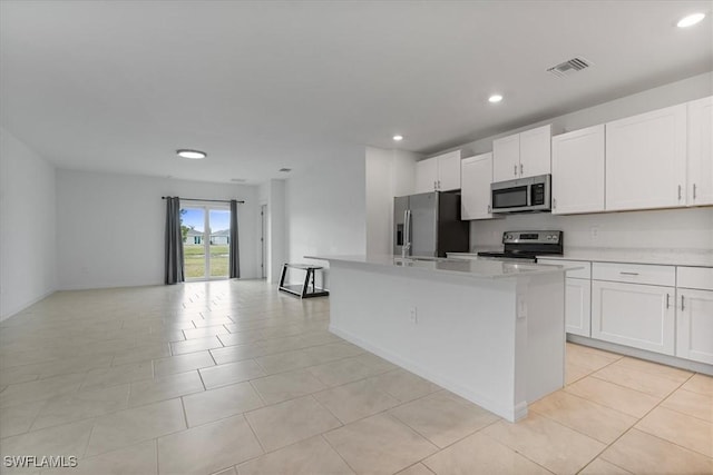 kitchen featuring light tile patterned floors, appliances with stainless steel finishes, an island with sink, and white cabinets