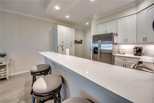 kitchen featuring a kitchen bar, white cabinetry, ornamental molding, stainless steel fridge, and kitchen peninsula