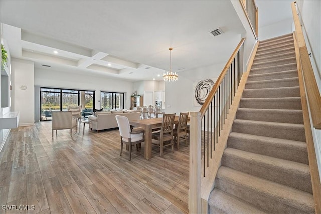 dining room featuring a notable chandelier, coffered ceiling, wood finished floors, visible vents, and stairway