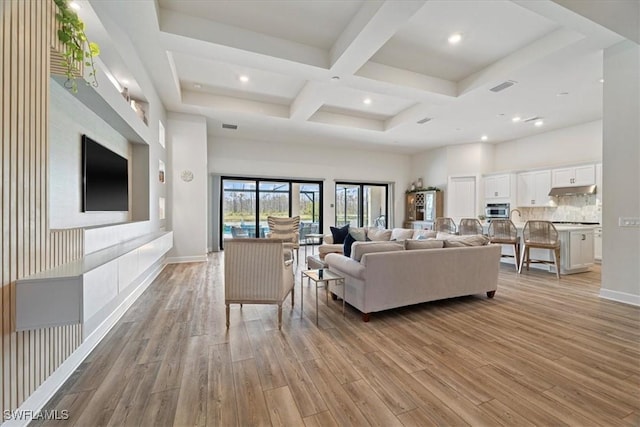 living room featuring visible vents, coffered ceiling, light wood finished floors, and a high ceiling