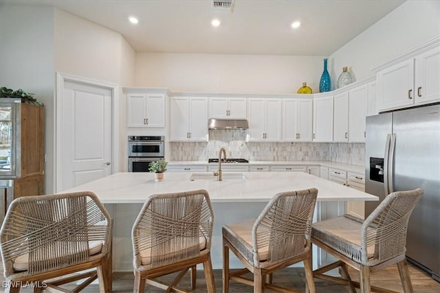 kitchen featuring visible vents, decorative backsplash, appliances with stainless steel finishes, an island with sink, and under cabinet range hood