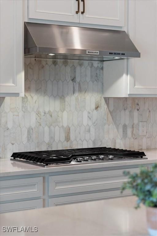 kitchen featuring under cabinet range hood, stainless steel gas cooktop, white cabinetry, light countertops, and decorative backsplash