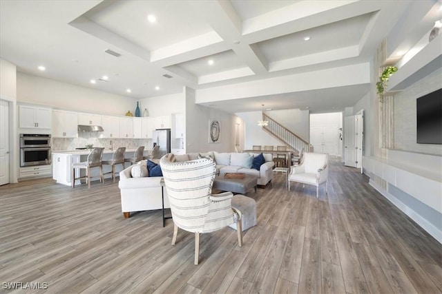 living room featuring coffered ceiling, visible vents, a towering ceiling, light wood-type flooring, and an inviting chandelier