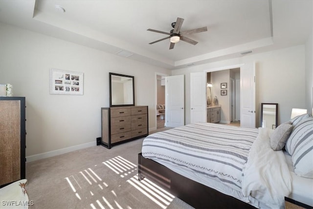 bedroom with ensuite bathroom, a raised ceiling, light colored carpet, and baseboards