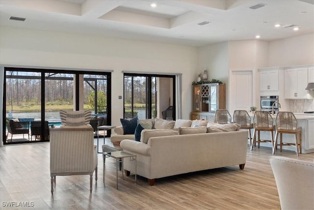 living area with visible vents, light wood-style flooring, and a towering ceiling