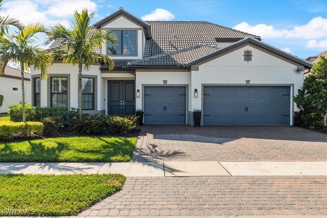 view of front facade with a garage, decorative driveway, a tile roof, and stucco siding