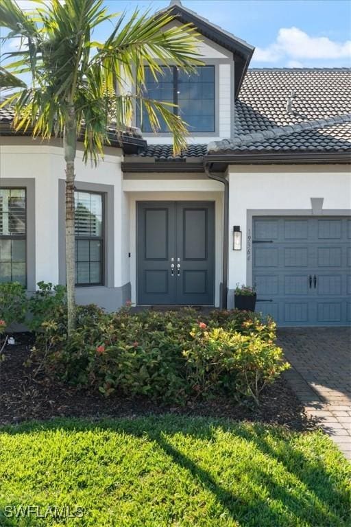 property entrance with an attached garage, a tile roof, decorative driveway, and stucco siding