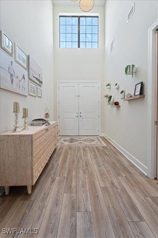 foyer featuring visible vents, a towering ceiling, light wood-style flooring, and baseboards