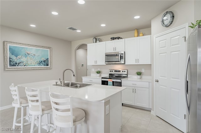 kitchen with appliances with stainless steel finishes, an island with sink, sink, white cabinets, and a kitchen breakfast bar