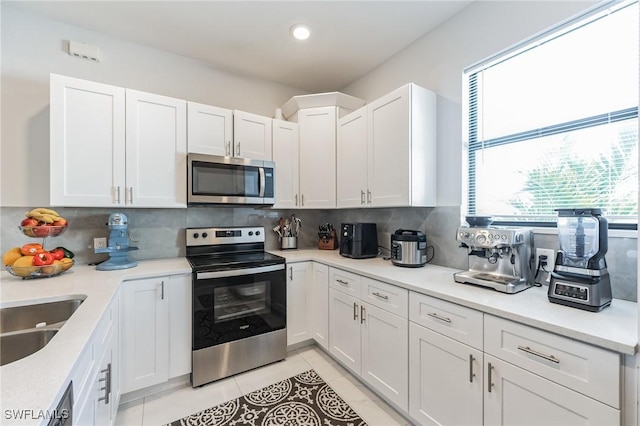 kitchen featuring light tile patterned flooring, appliances with stainless steel finishes, tasteful backsplash, white cabinetry, and sink