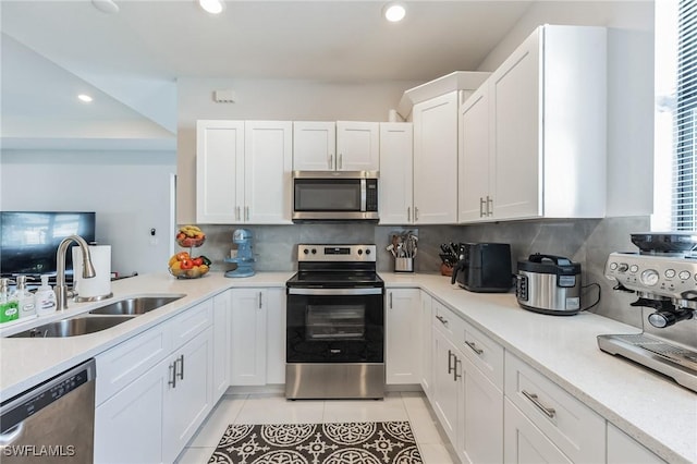 kitchen featuring light tile patterned flooring, appliances with stainless steel finishes, tasteful backsplash, sink, and white cabinets