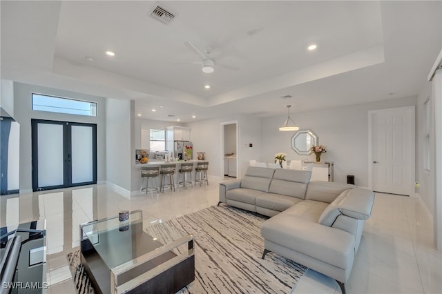 tiled living room with a raised ceiling, ceiling fan, and french doors