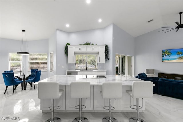 kitchen featuring hanging light fixtures, a breakfast bar area, light stone countertops, and white cabinets