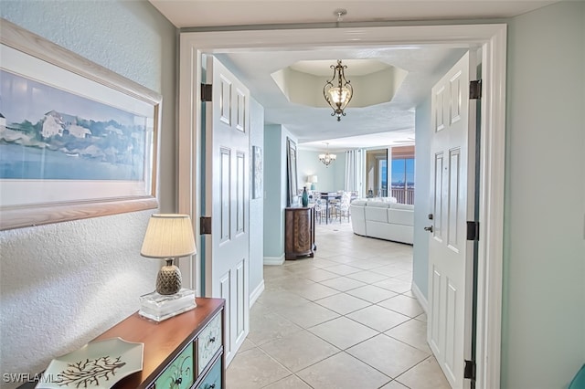 hall featuring an inviting chandelier, light tile patterned floors, and a raised ceiling