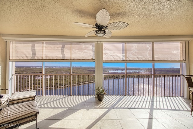 unfurnished sunroom featuring ceiling fan and a water view