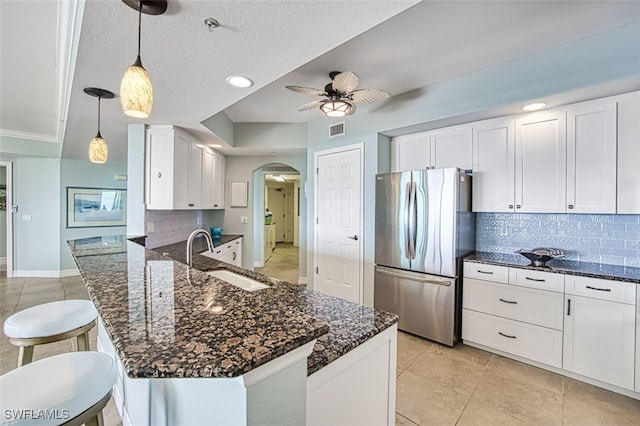 kitchen featuring stainless steel refrigerator, sink, backsplash, white cabinets, and hanging light fixtures