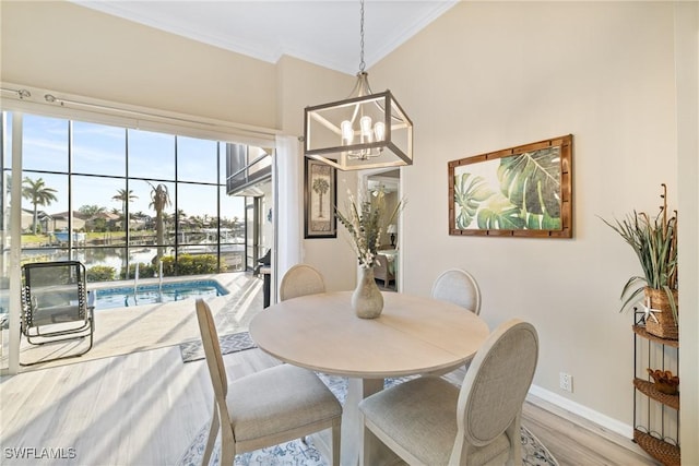 dining space with hardwood / wood-style flooring, ornamental molding, a water view, and an inviting chandelier