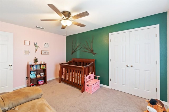 carpeted bedroom with ceiling fan, a closet, and a crib