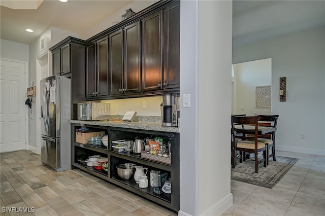 kitchen featuring light stone counters, dark brown cabinetry, and stainless steel fridge with ice dispenser