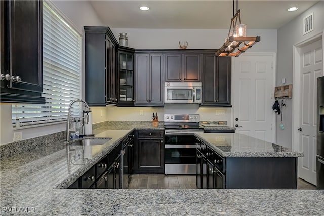 kitchen with pendant lighting, sink, stainless steel appliances, light stone countertops, and dark wood-type flooring