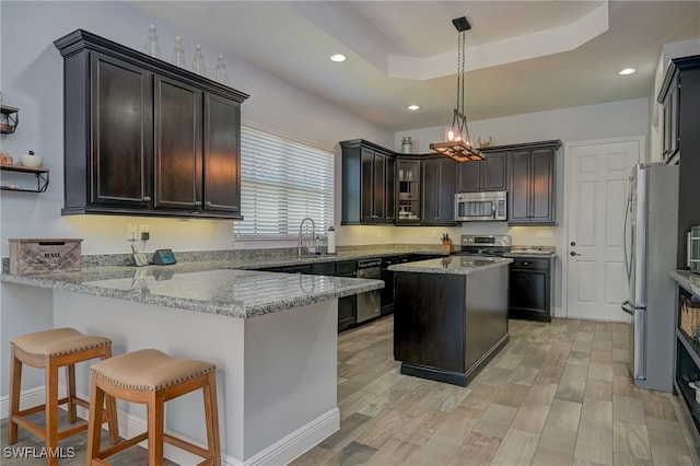 kitchen featuring a raised ceiling, kitchen peninsula, pendant lighting, stainless steel appliances, and light stone countertops