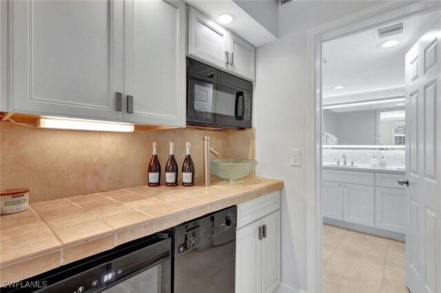 kitchen with sink, white cabinetry, black appliances, tile counters, and backsplash