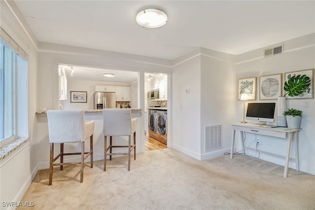 kitchen featuring white cabinetry, a breakfast bar area, kitchen peninsula, stainless steel appliances, and washing machine and dryer