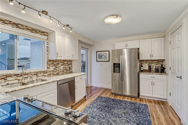 kitchen featuring appliances with stainless steel finishes, white cabinetry, sink, backsplash, and light stone counters