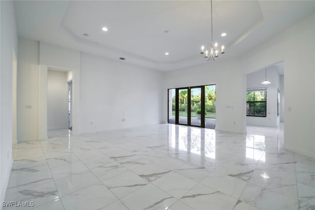 unfurnished room featuring a raised ceiling, a high ceiling, a notable chandelier, and french doors