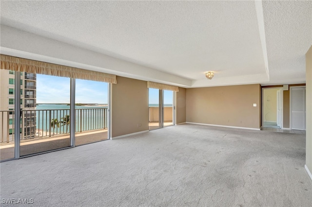 unfurnished room with carpet, a raised ceiling, a textured ceiling, and a water view