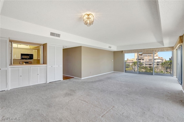 unfurnished living room with carpet flooring, a textured ceiling, and a tray ceiling