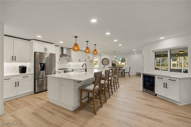 kitchen with appliances with stainless steel finishes, white cabinets, decorative light fixtures, a large island with sink, and wine cooler