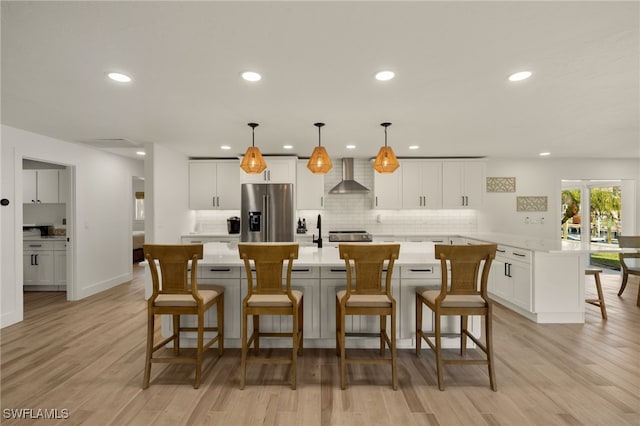 kitchen featuring a center island, white cabinetry, high end fridge, pendant lighting, and wall chimney range hood