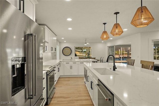 kitchen with high end appliances, light wood-type flooring, white cabinets, pendant lighting, and sink