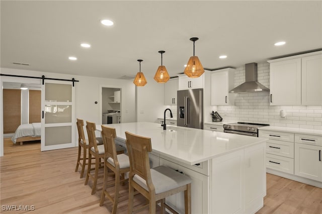 kitchen with washing machine and dryer, a center island with sink, stainless steel appliances, a barn door, and wall chimney exhaust hood