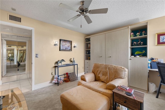 living area featuring a textured ceiling, light carpet, visible vents, baseboards, and a ceiling fan