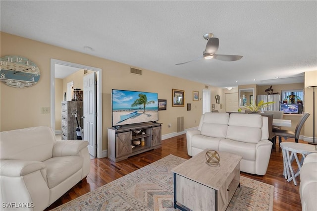 living room with baseboards, a textured ceiling, visible vents, and wood finished floors