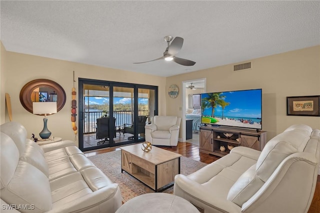 living area featuring a textured ceiling, wood finished floors, visible vents, and a ceiling fan