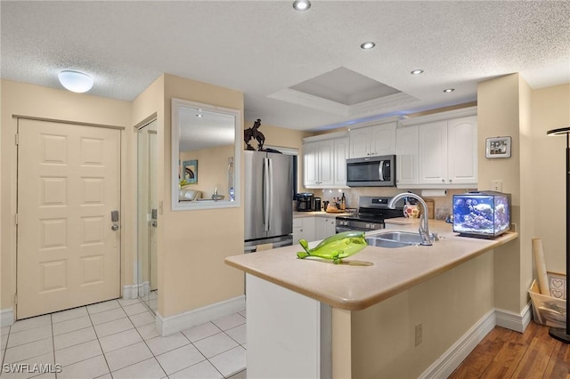 kitchen with a peninsula, stainless steel appliances, light countertops, white cabinetry, and a sink