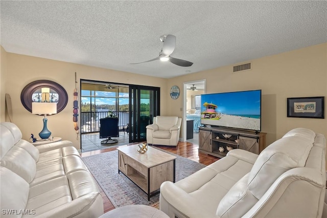 living room featuring visible vents, ceiling fan, a textured ceiling, and wood finished floors