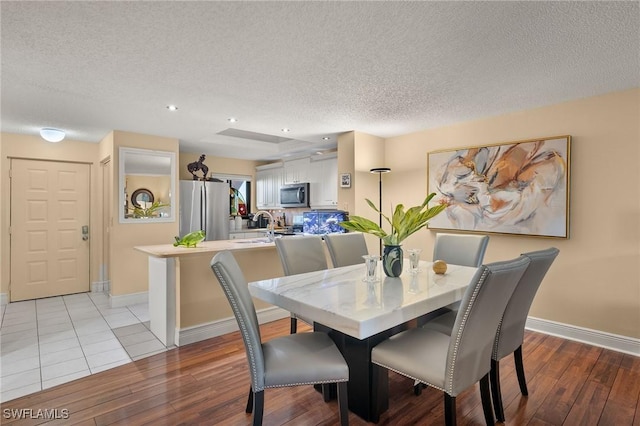 dining space with baseboards, a textured ceiling, and light wood finished floors