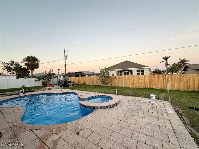 pool at dusk with an in ground hot tub, a patio area, and a lawn