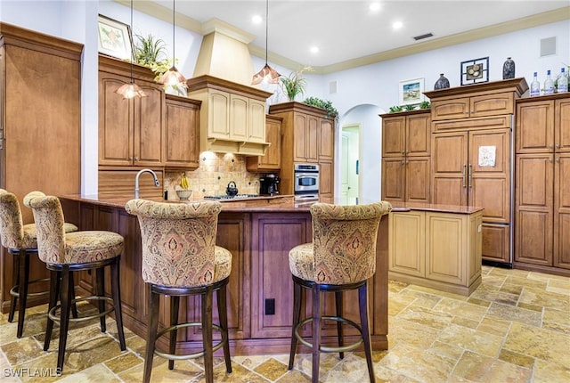 kitchen featuring an island with sink, a breakfast bar, light stone counters, and decorative light fixtures