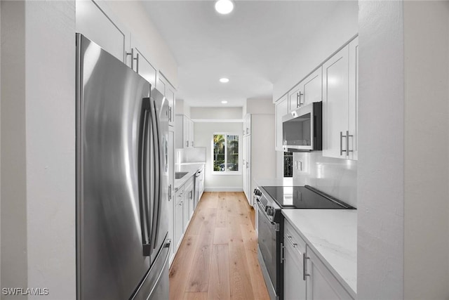 kitchen with white cabinets, light wood-style flooring, light stone counters, and stainless steel appliances