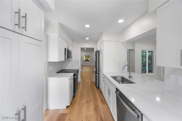 kitchen with appliances with stainless steel finishes, light stone countertops, light wood-type flooring, white cabinetry, and a sink