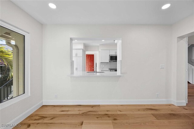 interior space featuring recessed lighting, wood finished floors, baseboards, white cabinets, and stainless steel microwave