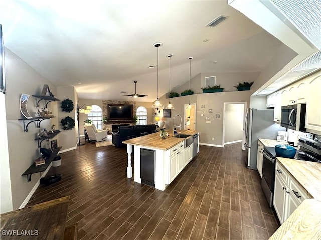 kitchen with appliances with stainless steel finishes, wood counters, white cabinets, hanging light fixtures, and a kitchen island with sink